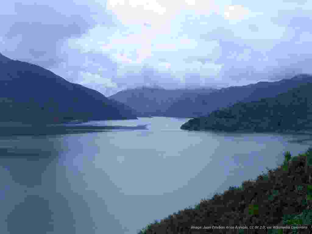 Wide view of the blue water of the Salvajina Resservoir, and the green-covered mountains surrounding it